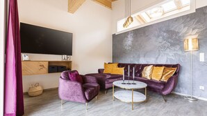 Ein modernes Wohnzimmer mit einem violetten Sofa, zwei runden Tischen und einem großen, an der Wand befestigten Fernseher.