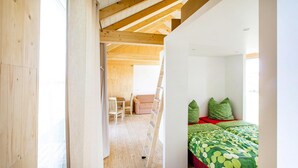 A bedroom with a wooden ceiling, a bed with green and red bedding, and a small seating area with a chair and a table. - Camp David Sport Resort (Rackwitz)