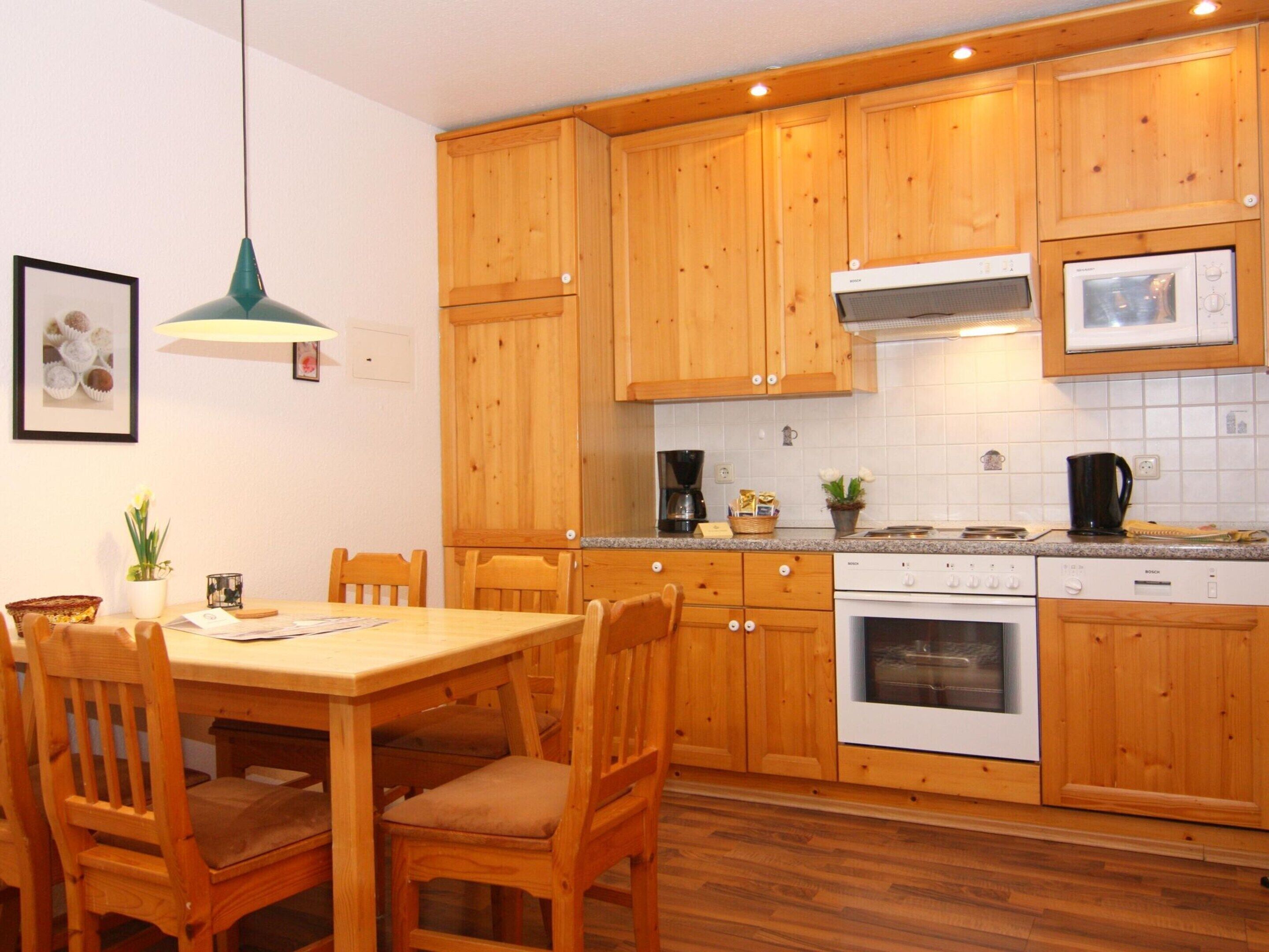 A kitchen with wooden cabinets, a dining table with chairs, a coffee maker, and a Bosch oven.