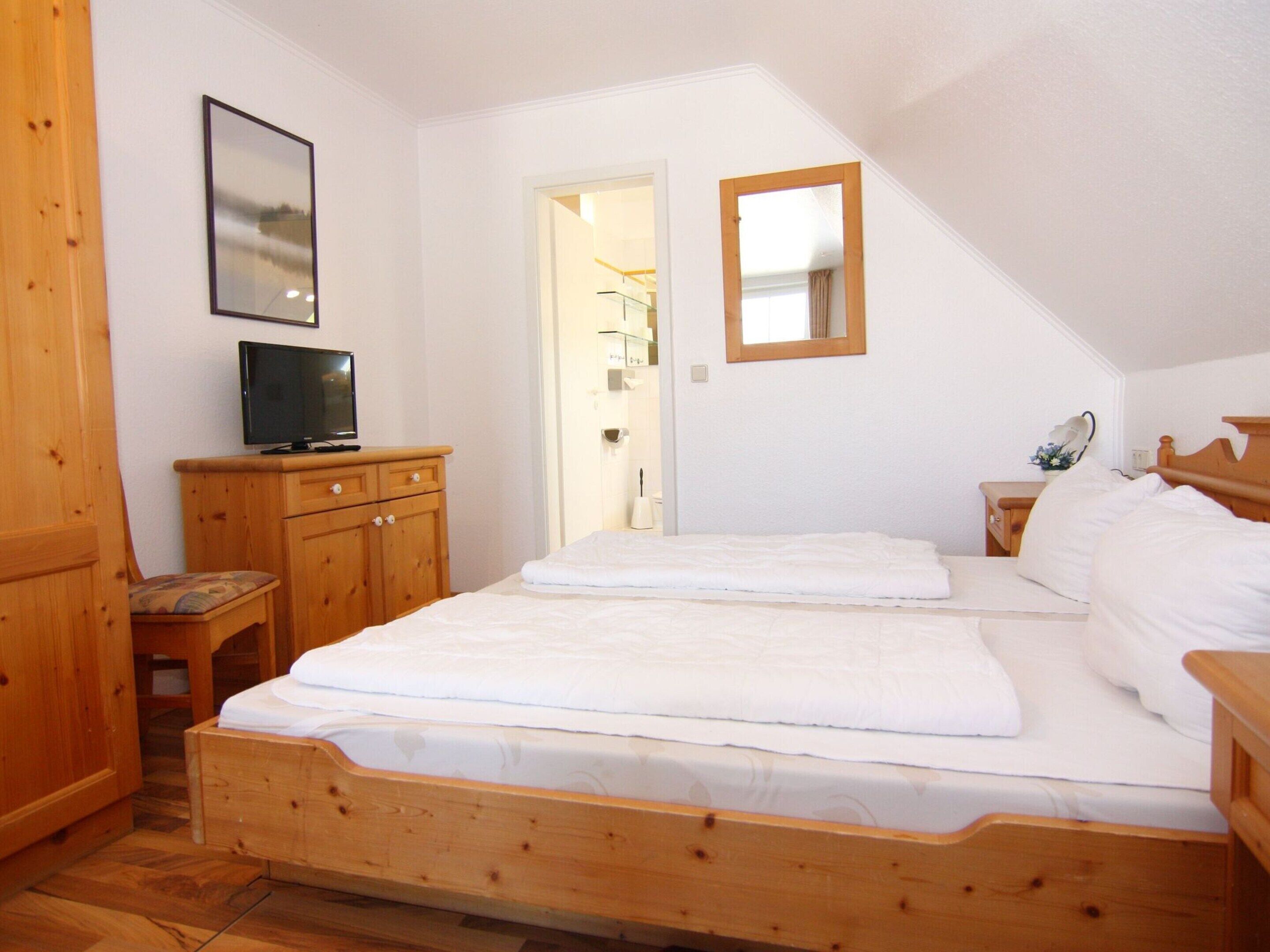 A bedroom with a wooden bed, a television on a wooden dresser, and a mirror on the wall.