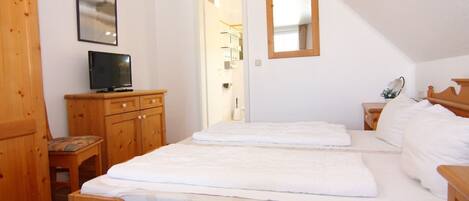 A bedroom with a wooden bed, a television on a wooden dresser, and a mirror on the wall.
