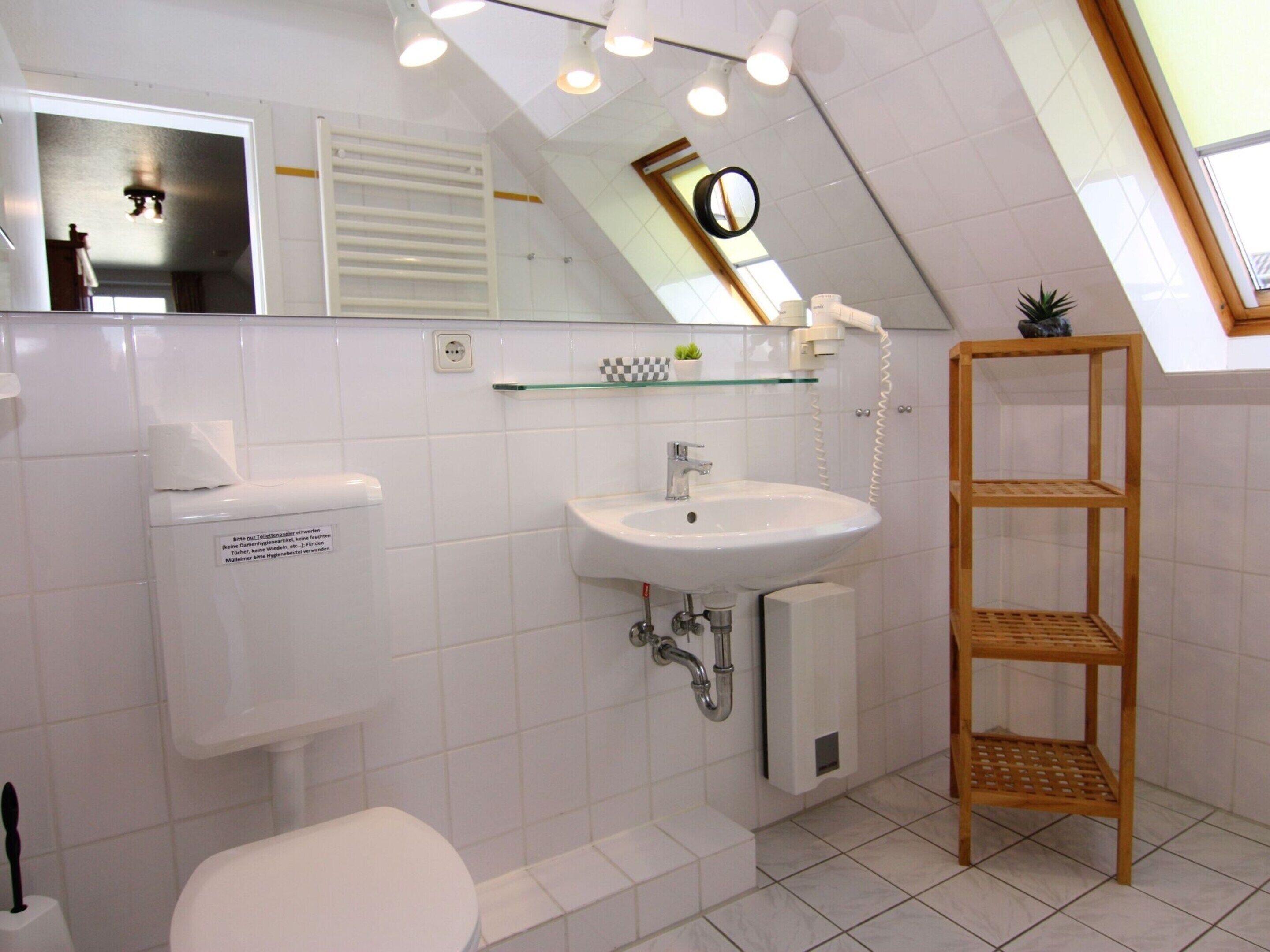 A bathroom with a toilet, sink, and wooden shelf.