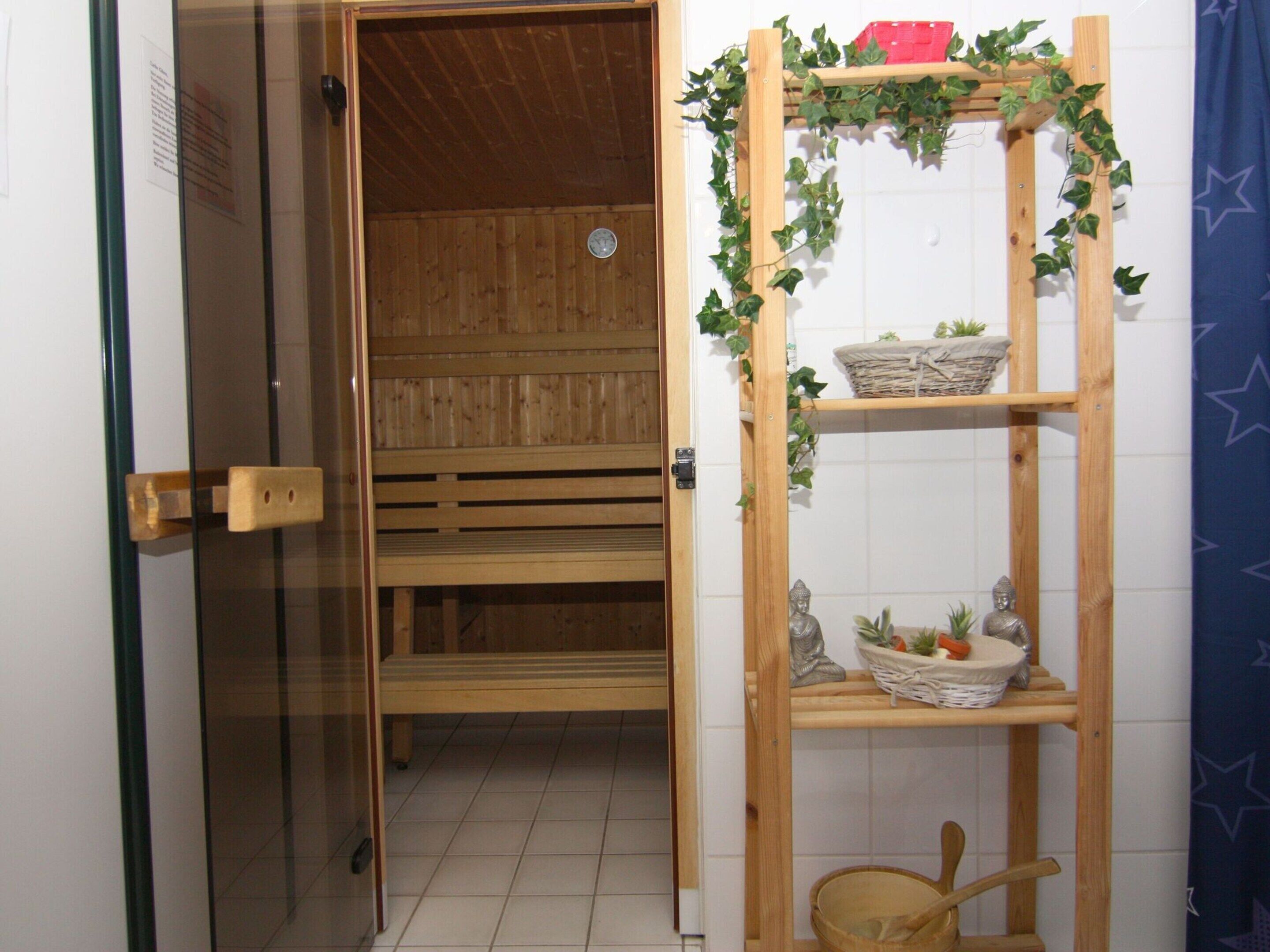 A wooden sauna with benches, a wooden shelf with baskets and plants, and a tiled floor.