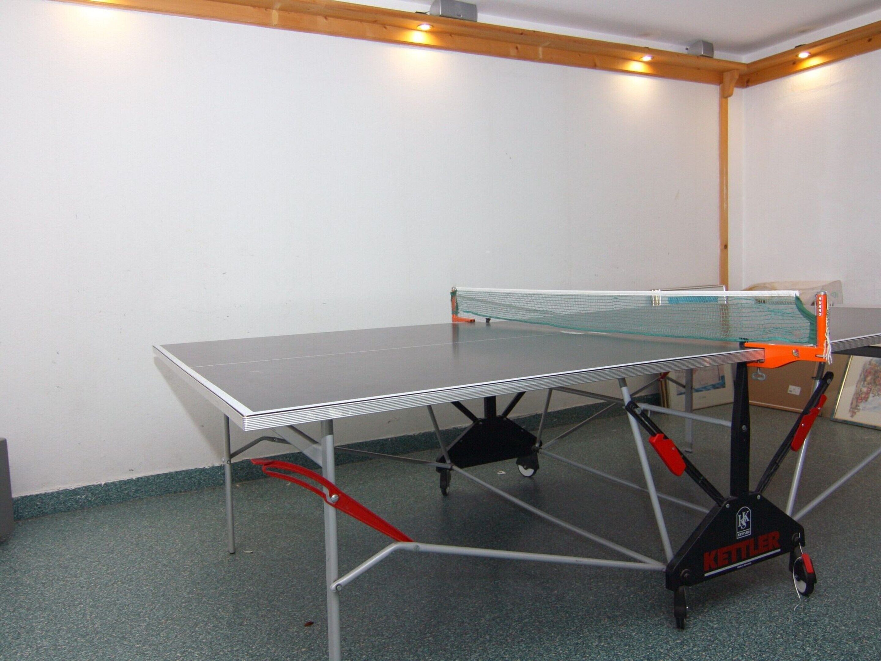 Ein Tischtennistisch mit Netz in einem Raum mit grünem Teppich und weißen Wänden.