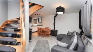 A compact living space with a wooden staircase, a dining area with a table and chairs, a sofa, and a small kitchen area with a stove. - Comfortable Holiday Homes by the Sea, Jaroslawiec (Postomino)