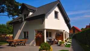 A two-story house with a patio area featuring wooden benches and a flower bed. - Comfortable Holiday Homes by the Sea, Jaroslawiec (Postomino)