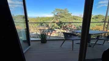 A balcony with a table and chairs, a potted plant, and a view of trees and buildings.