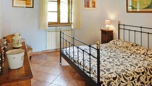 A bedroom with a bed, a nightstand, a lamp, a window with curtains, and a radiator. - Holiday Home Villa del Pino, Massarosa (Massarosa)