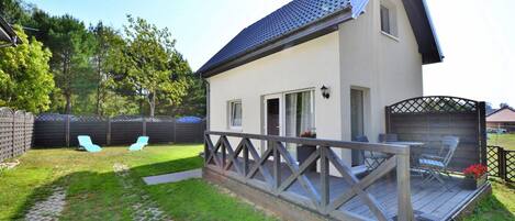 A house with a covered patio, a fenced backyard, and a small deck with chairs.