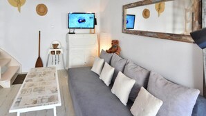 Una sala moderna con un sofá gris, una mesa blanca con estampado de periódico, un televisor sobre un mueble de madera y un espejo con marco rústico.