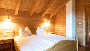Een slaapkamer in een houten chalet, met een bed, twee nachtkastjes en wandlampen.