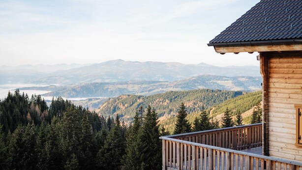 Een houten chalet met een balkon met uitzicht op een bebost berglandschap.