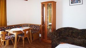 A dining area with a wooden table and chairs, a patterned sofa, and a cabinet with glass doors. - Sunny Holiday Apartment on Lake Klopeiner With Balcony and Private Beach (Sankt Kanzian am Klopeiner See)