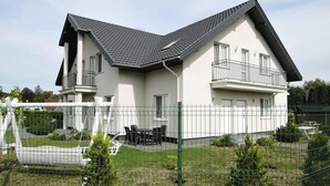 Kaksikerroksinen talo, jossa on kalteva katto, parveke ylemmässä kerroksessa ja aidattu piha, jossa on pieni patio.