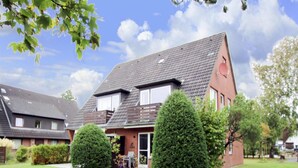 Ein zweistöckiges Haus mit geneigtem Dach, einer Ziegel-Fassade und einem gepflegten Rasen mit zwei geschnittenen Büschen.
