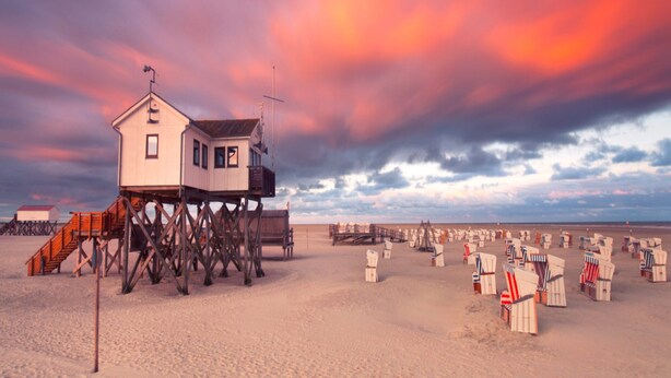 Ein Strandhaus auf Stelzen mit Blick auf den Ozean und Liegestühle.