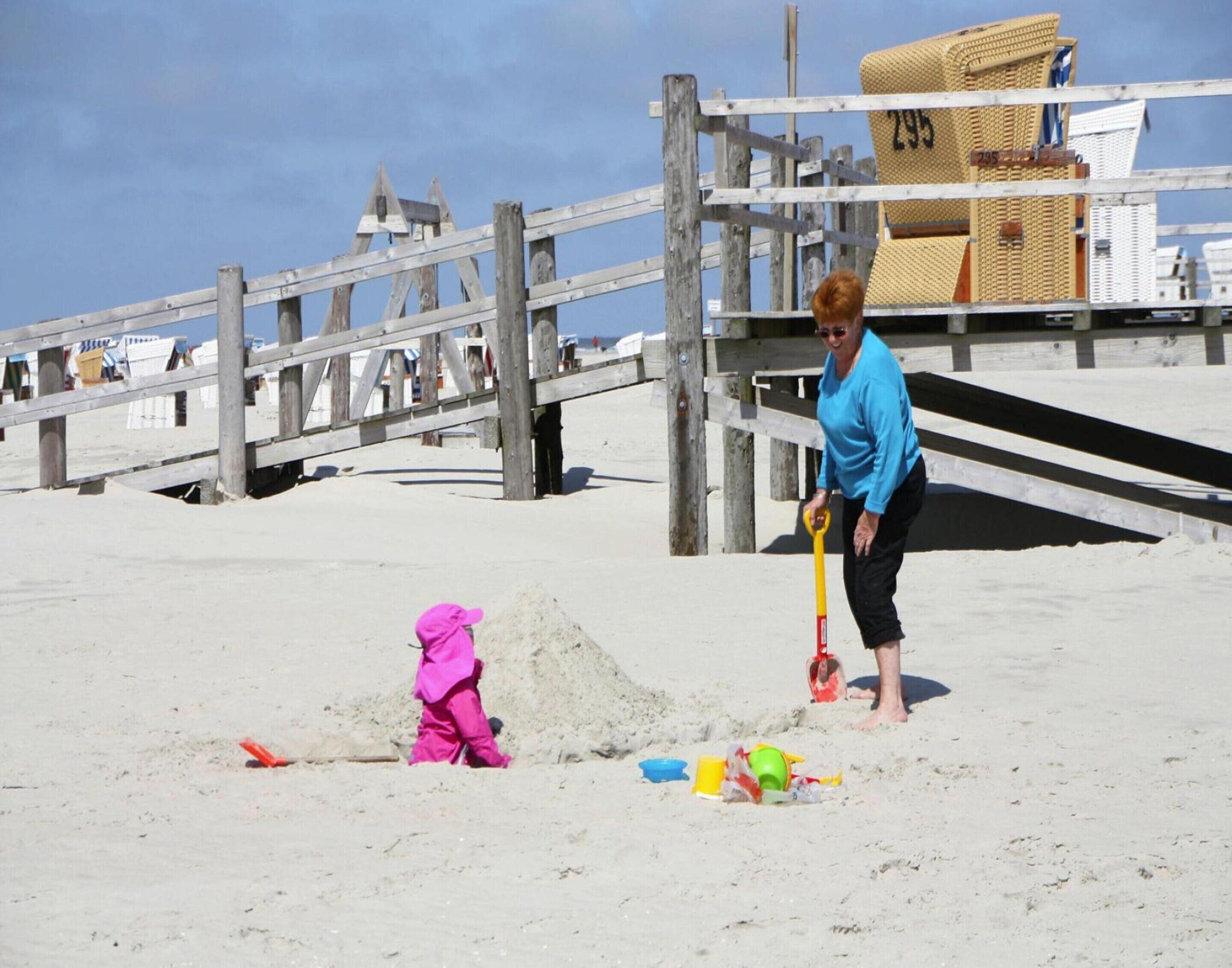 A beach with a wooden fence, a lifeguard tower, and a person and child playing with sand toys.