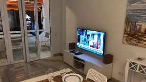 Ein Essbereich mit einem Fernseher, der einen Nachrichtensender zeigt, einem weißen Tisch mit Unterlage und einem Stuhl.
