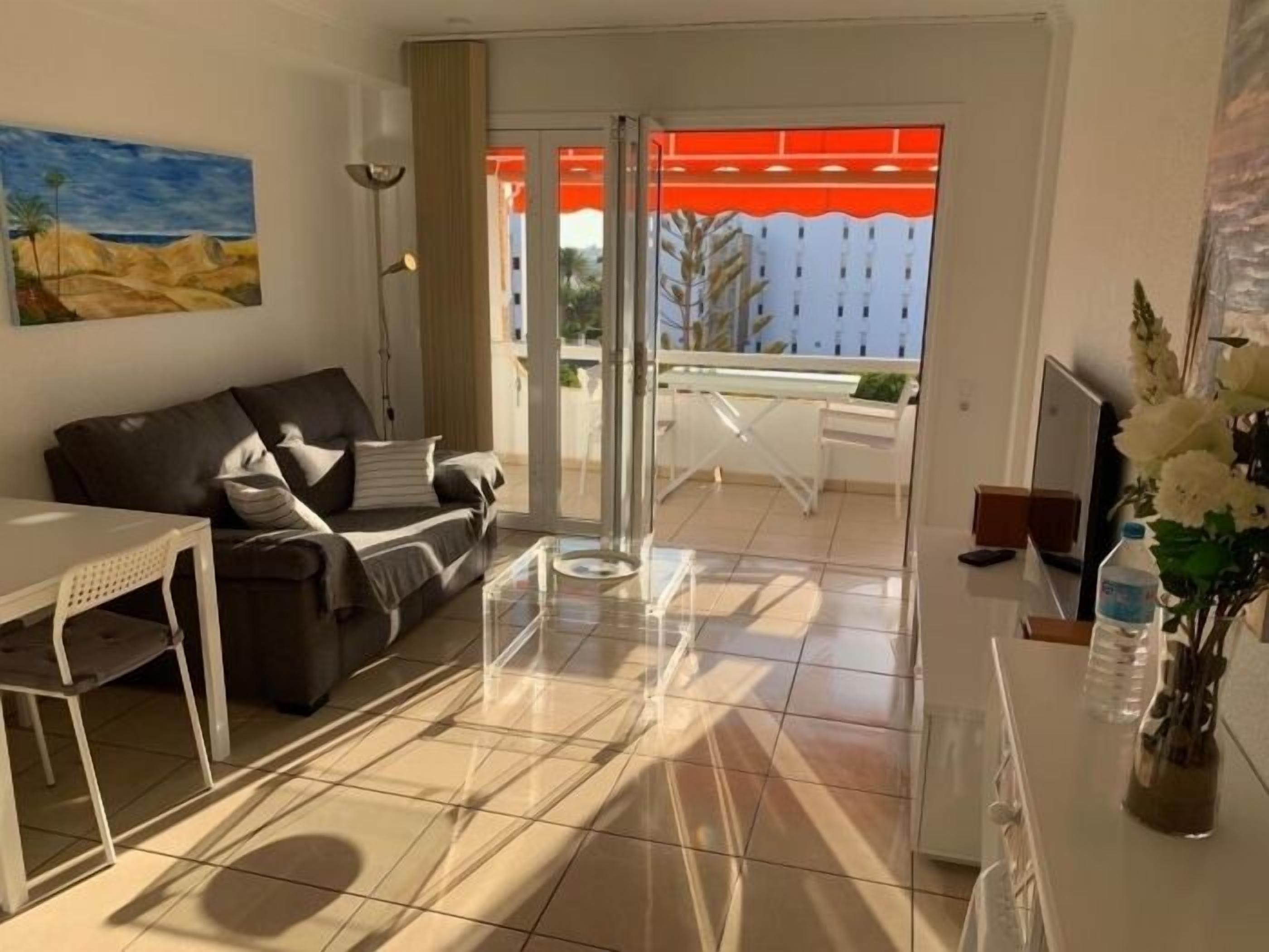 A modern living room with a sofa, a dining table, and a balcony with a red awning.