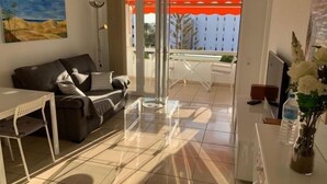 Ein modernes Wohnzimmer mit einer Couch, einem Esstisch und einem Balkon mit rotem Markisenvorhang.
