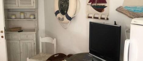 Una habitación pequeña con una televisión, una silla, una mesa y un adorno de salvavidas en la pared.
