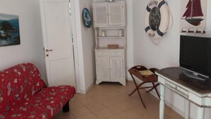 A room with a red patterned sofa, a white cabinet, a television on a wooden table, and a door. - Apartment in Sardinia Near Surf Paradise (Palau)