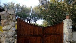 A rustic wooden gate with a stone wall on one side and a tree-lined background. - Apartment in Sardinia Near Surf Paradise (Palau)