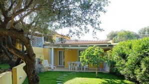 A yellow building with a patio area, stone pathway, and a tree. - Apartment in Sardinia Near Surf Paradise (Palau)