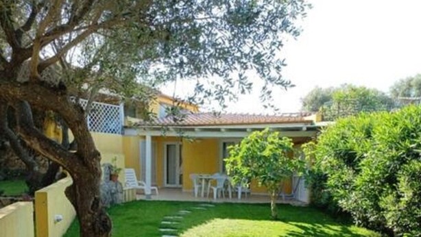 A yellow building with a patio area, stone pathway, and a tree. - Apartment in Sardinia Near Surf Paradise (Palau)