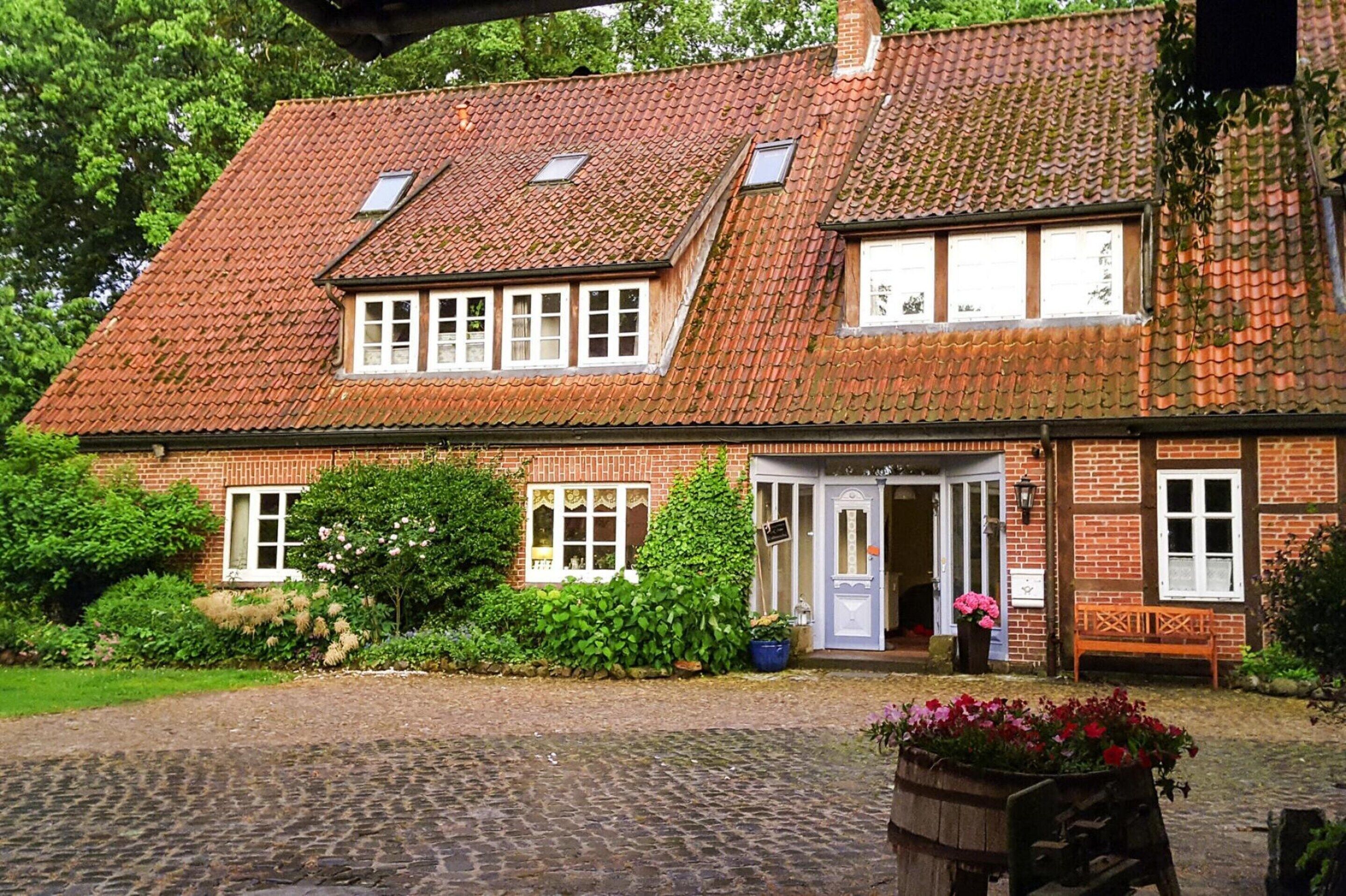 A traditional brick building with a tiled roof, a central entrance, and a cobblestone driveway.