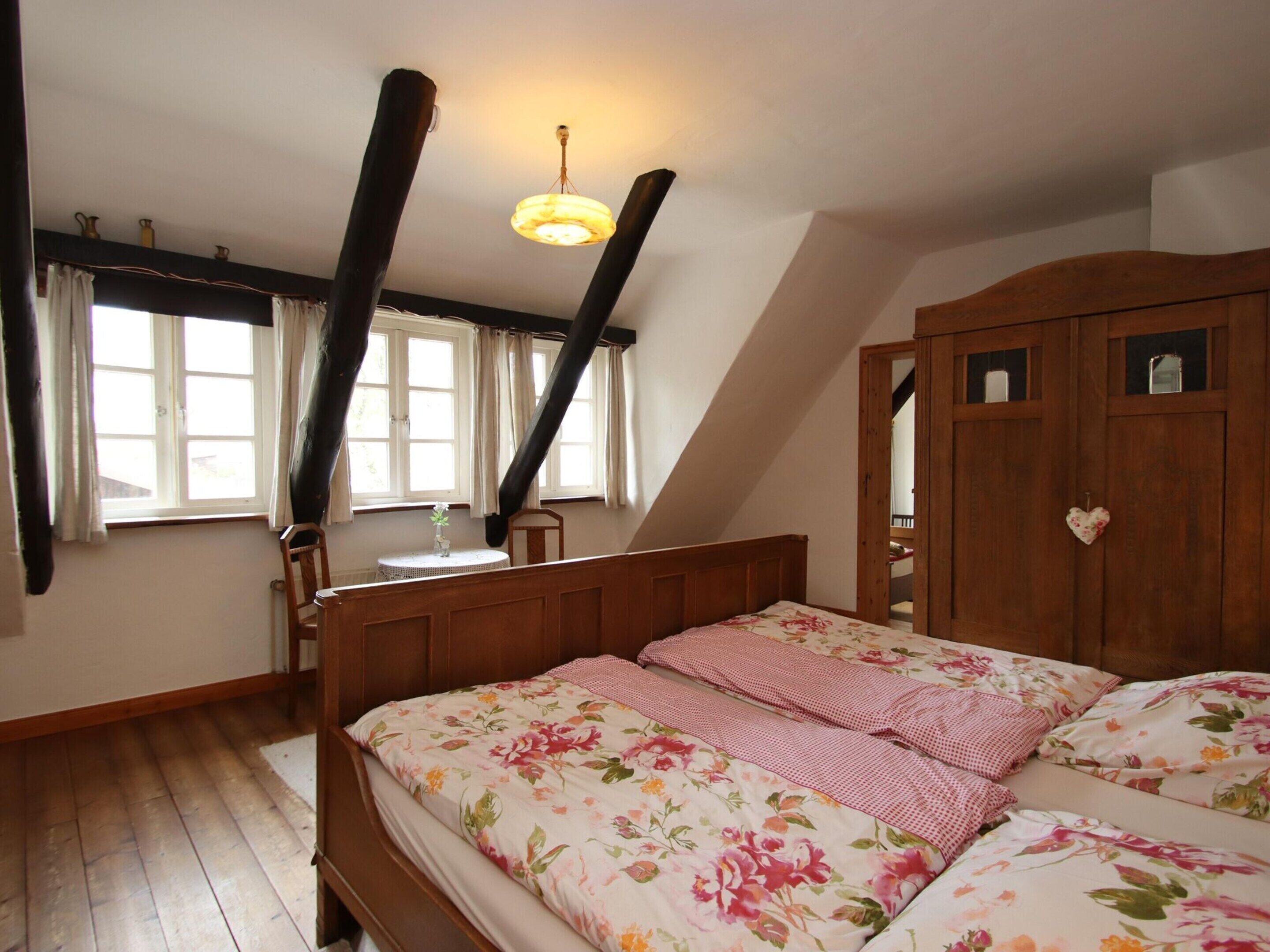 Un dormitorio con cama de madera, una mesita de noche, una ventana con cortinas y un armario de madera.