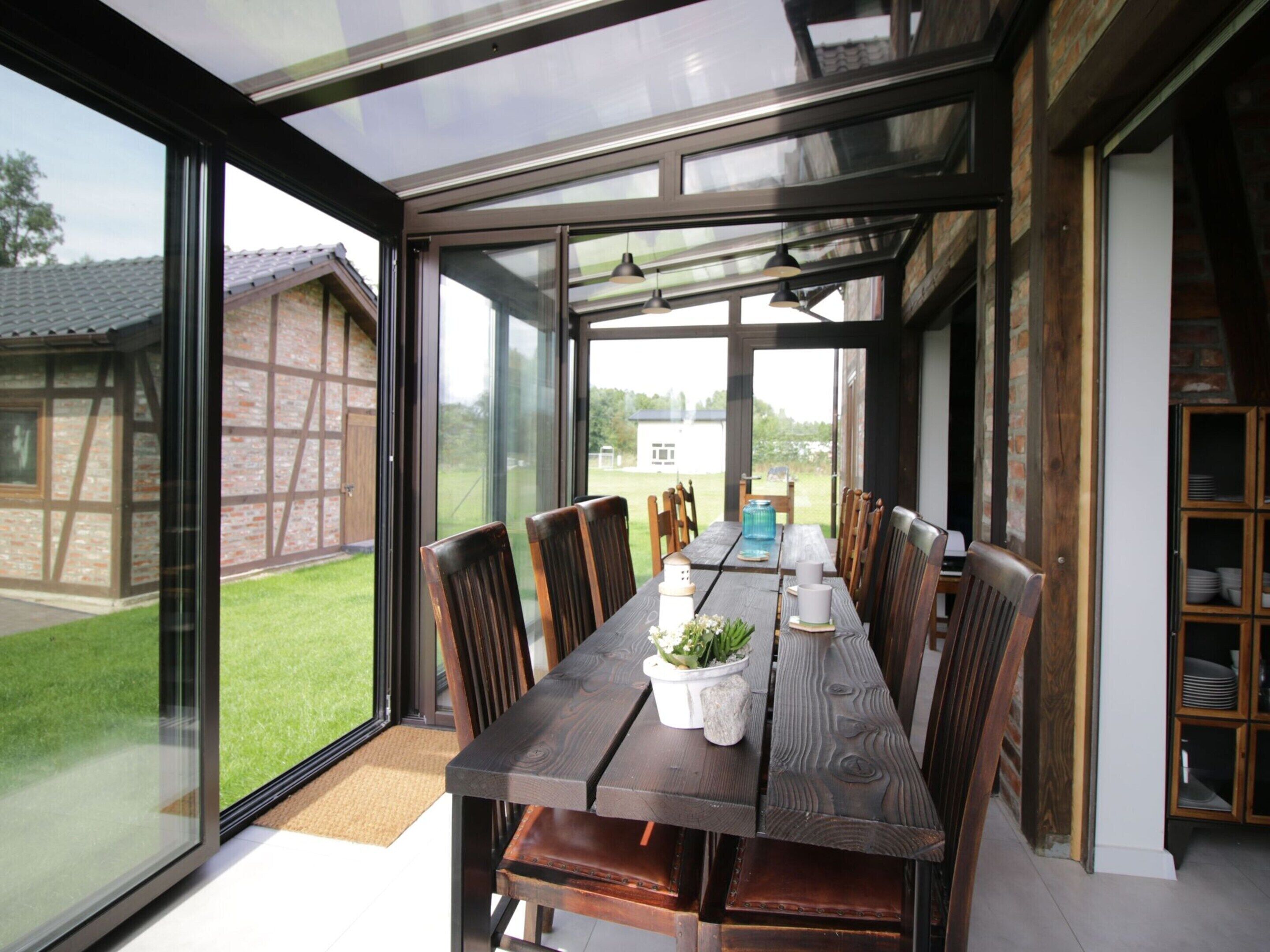 A modern dining area with a large table and chairs, a glass enclosure, and a view of the outdoors.
