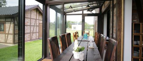 A modern dining area with a large table and chairs, a glass enclosure, and a view of the outdoors.