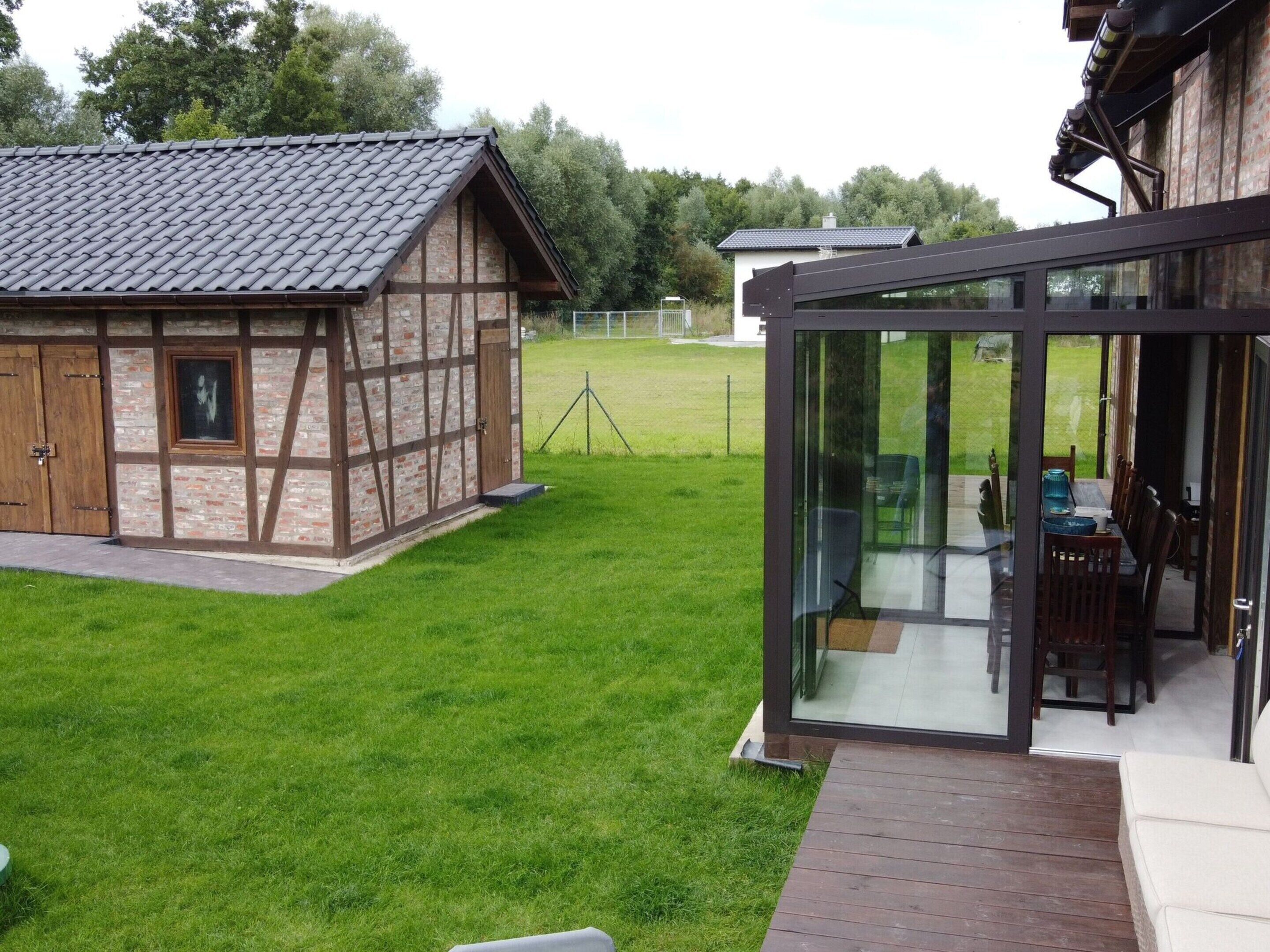 A modern house with a glass-enclosed patio, a traditional wooden structure, and a well-maintained lawn.