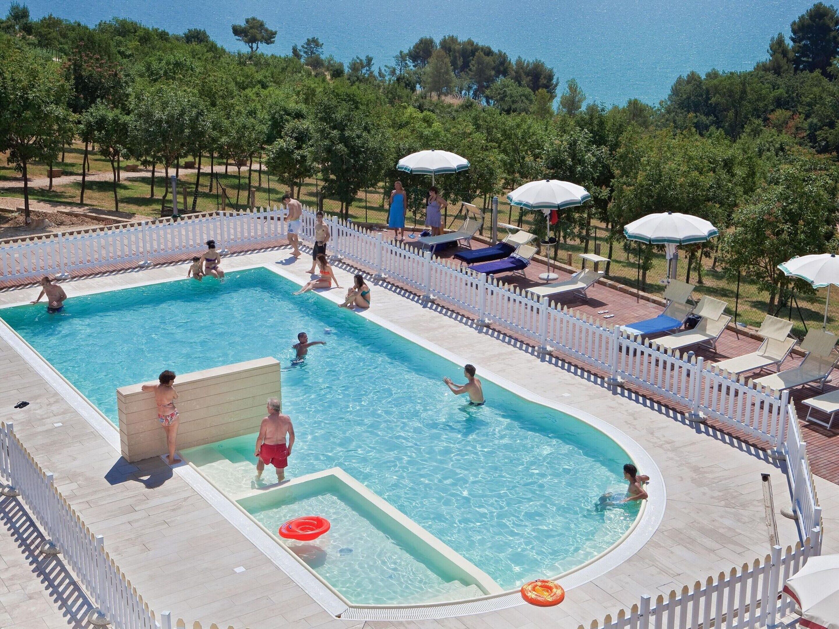 A swimming pool with a white fence, lounge chairs, and umbrellas.