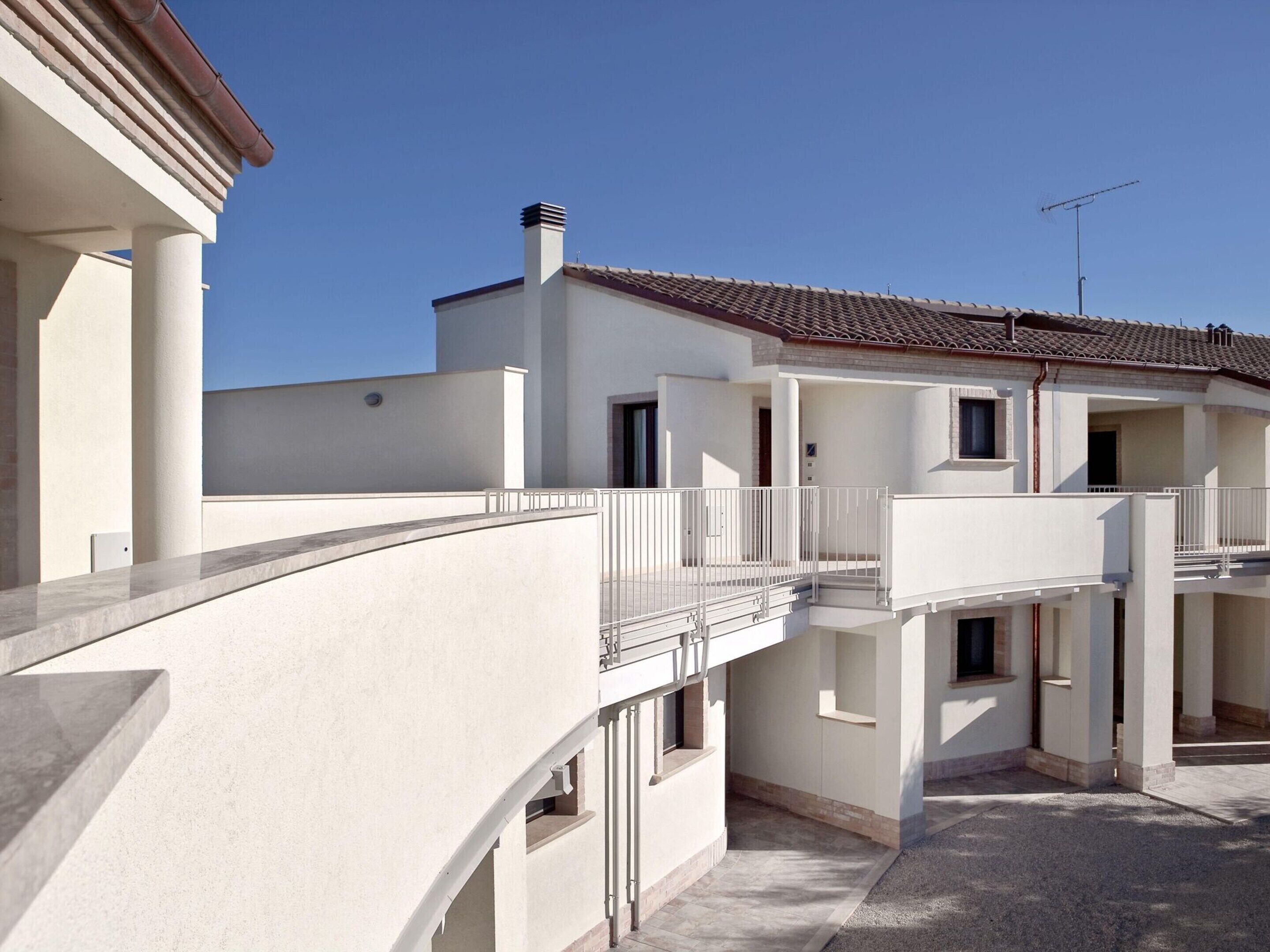 Un immeuble résidentiel à plusieurs étages, à l’extérieur blanc, avec un toit en tuiles et un balcon doté d’une rambarde en métal.
