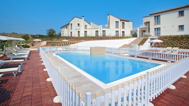 A swimming pool surrounded by white fences, with lounge chairs and umbrellas on a wooden deck. - Holiday Resort Contea dei Ciliegi, Pedaso (Pedaso)