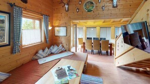 Interior acolhedor de uma cabana, com teto de madeira, área de refeições e cama com almofadas listradas.