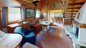 Interior acolhedor de uma cabana, com decoração em madeira, lareira, área de refeições e sala de estar com vista para o exterior.