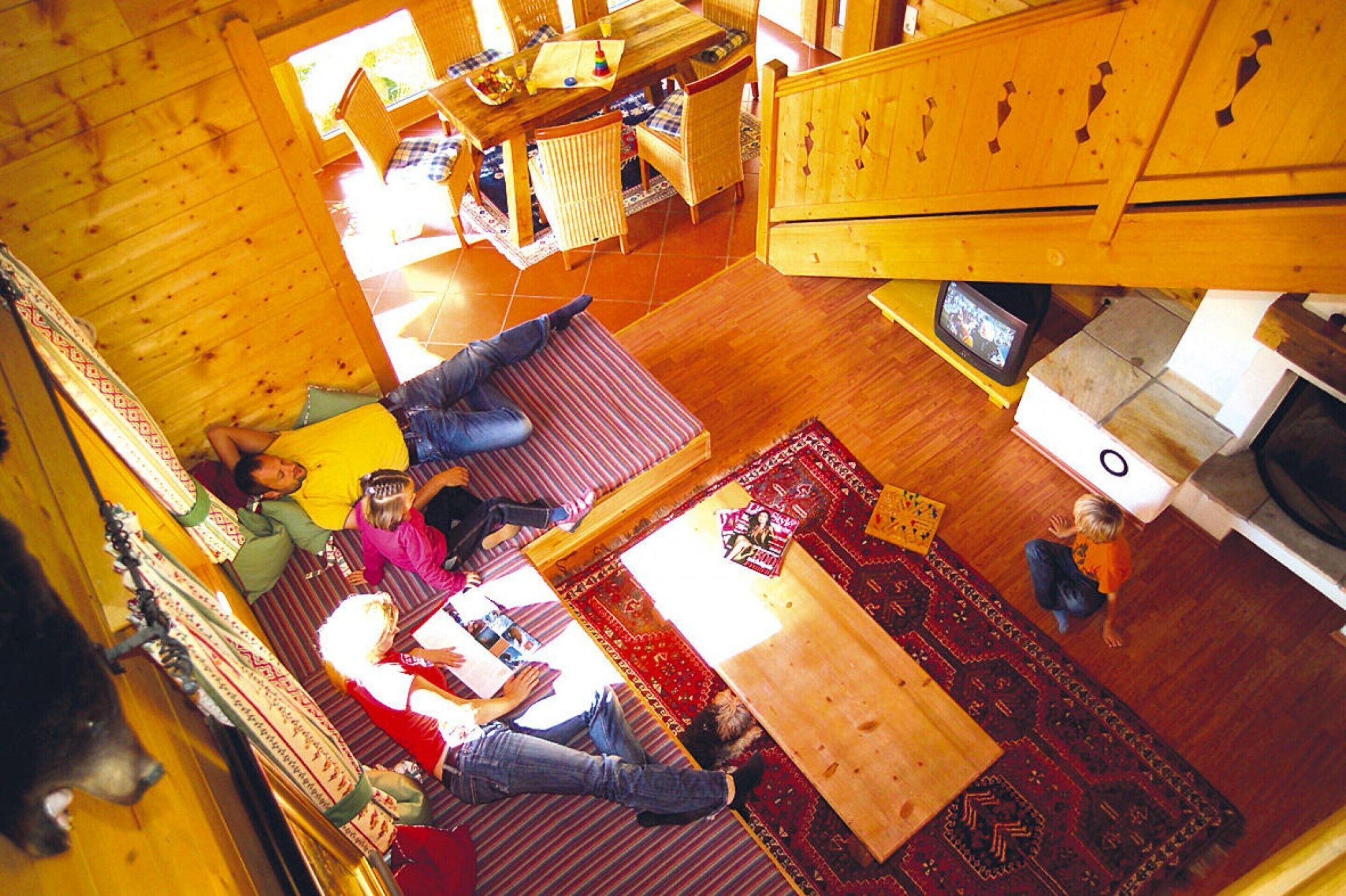 Een gezellig chaletinterieur met houten wanden en vloeren, een eethoek met stoelen en een tafel, en een televisie in de hoek.