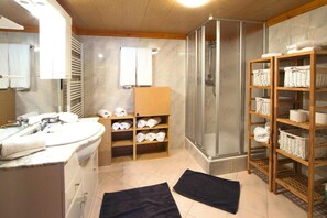 A bathroom with a sink, mirror, towel rack, shower, and shelves with towels and baskets. - Chalet in Wildkogel Near ski Slopes (Neukirchen am Grossvenediger)