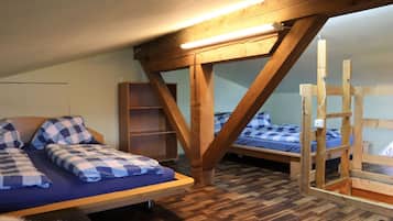 A dormitory room with two bunk beds, wooden beams, a bookshelf, and a fur rug.