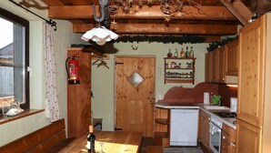 A rustic kitchen with wooden cabinets, a small refrigerator, and a dining table with a bowl of fruit and a bottle of wine. - Cabin in Brixental by Ski Lift Access (Mittersill)