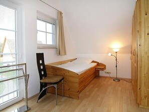 Un apartamento pequeño de una sola habitación con una cama nido de madera, un escritorio con silla, una lámpara de pie y una ventana con cortinas.