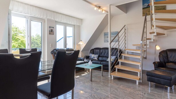 Ein modernes Wohnzimmer mit einem schwarzen Ledersofa, einem Esstisch und einer Treppe mit Holzvertäfelung.
