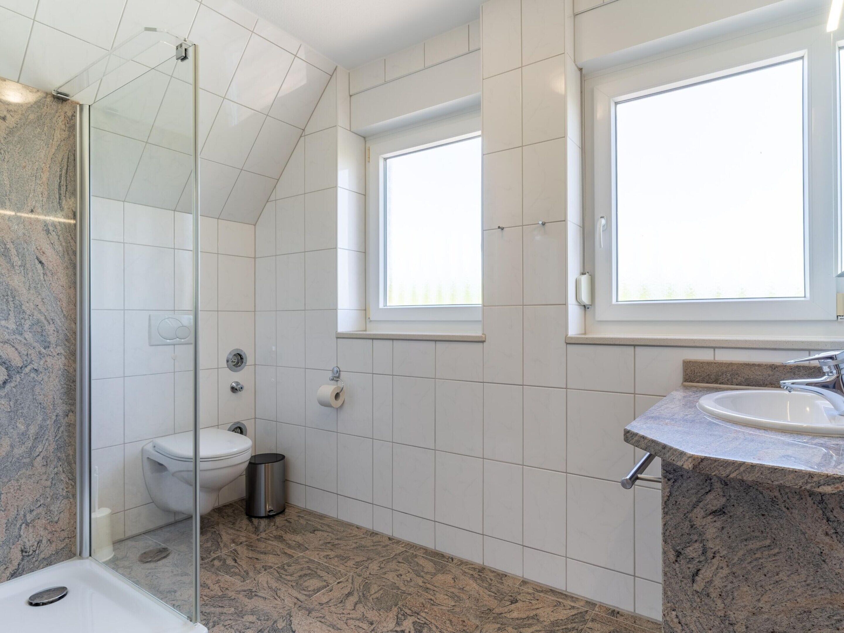 A modern bathroom with a glass-enclosed shower, a toilet, and a sink with a granite countertop.