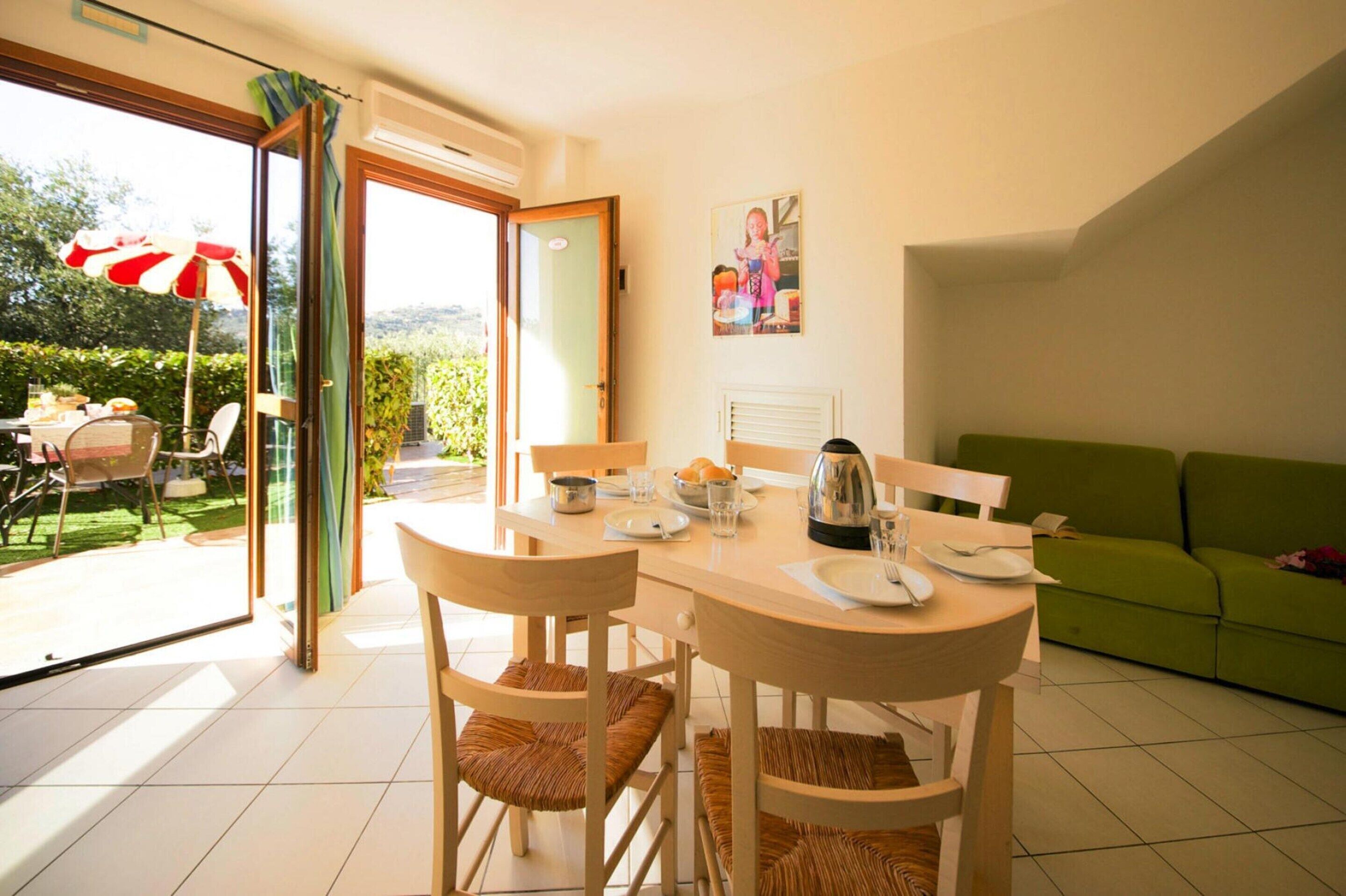 A dining area with a table set for two, chairs, a green sofa, and a sliding glass door leading to a garden.