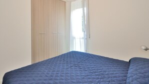 A bedroom with a bed, a wardrobe, and a window with curtains. - Apartment in Bibione Near the Beach (San Michele al Tagliamento)