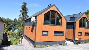 Une maison moderne à deux étages, dotée d’une façade en bois, de grandes fenêtres et d’un toit à pente.