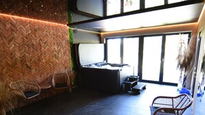 Un intérieur moderne avec un mur orné d’un motif en chevrons, un coin salon avec des fauteuils en osier, une petite table et une grande fenêtre laissant entrer la lumière naturelle.